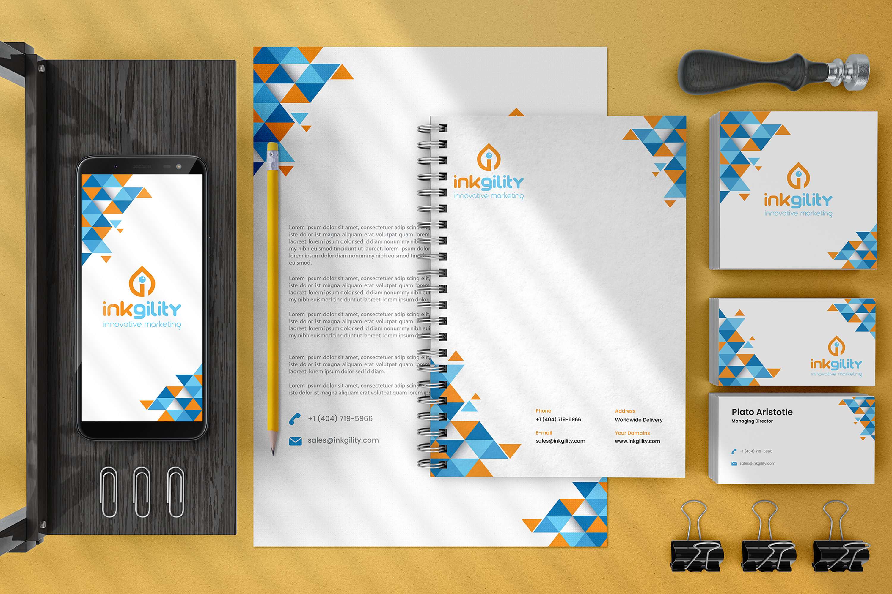 Inkgility blue and orange triangle pattern stationery on yellow ground: phone with app splash, letterhead, spiral notebook, two business cards, binder clips, and phone with brand mark