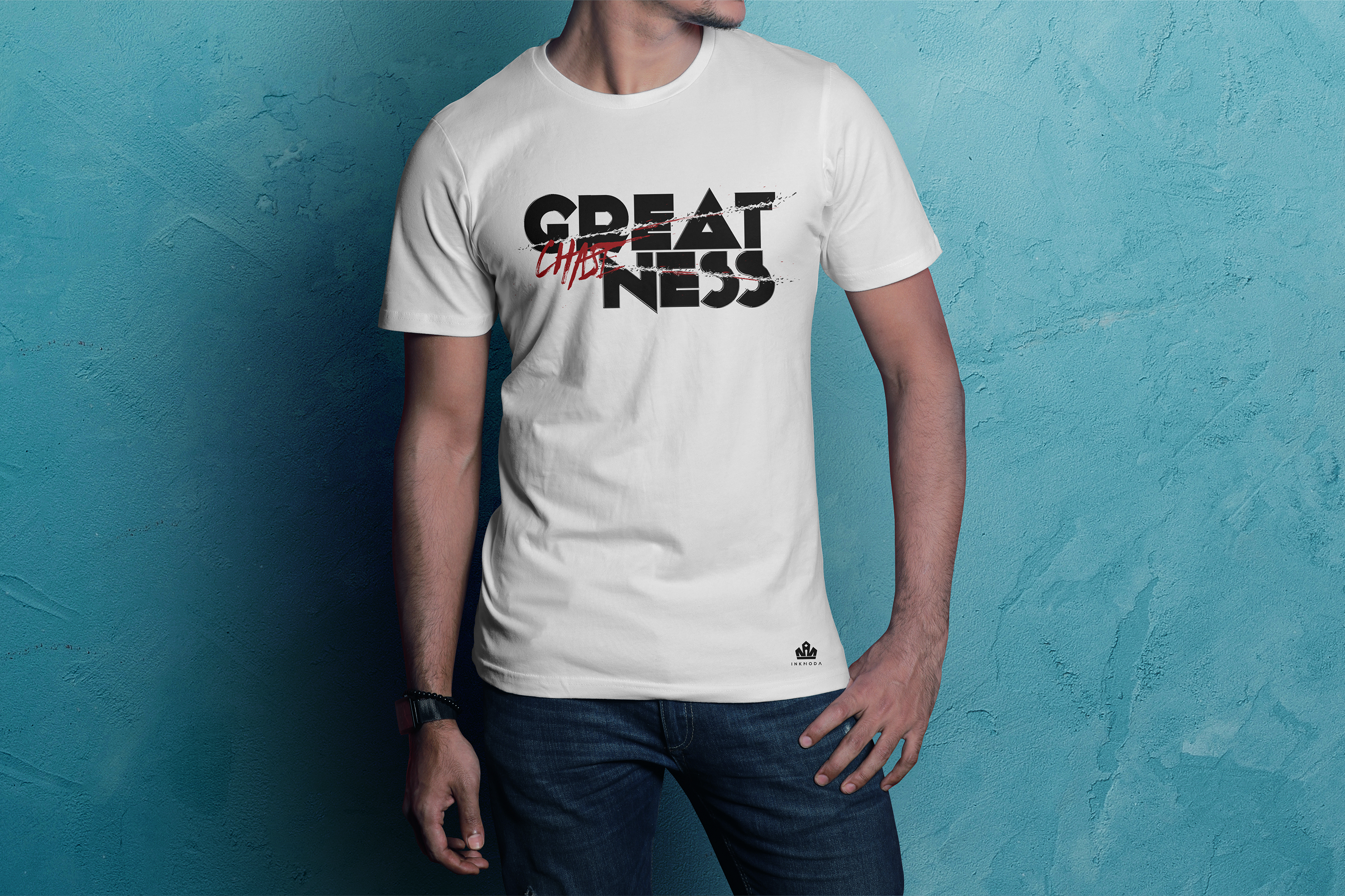 Male model in white Inknoda tee against teal painted wall wearing the GREATNESS typographic design with CHASE struck through in a red brush stroke, denim jeans